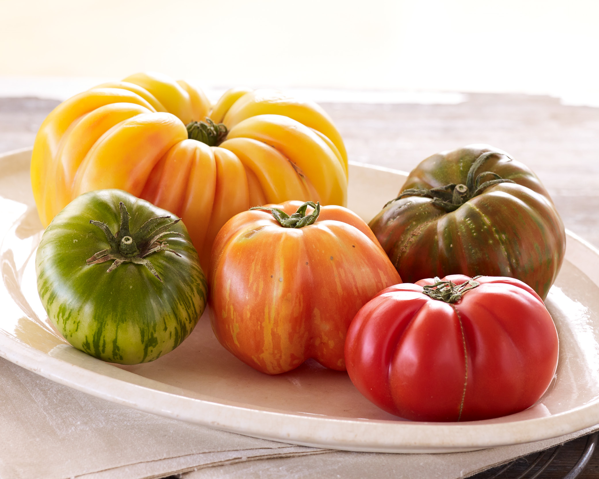 5 heirloom tomatoes on a white plate