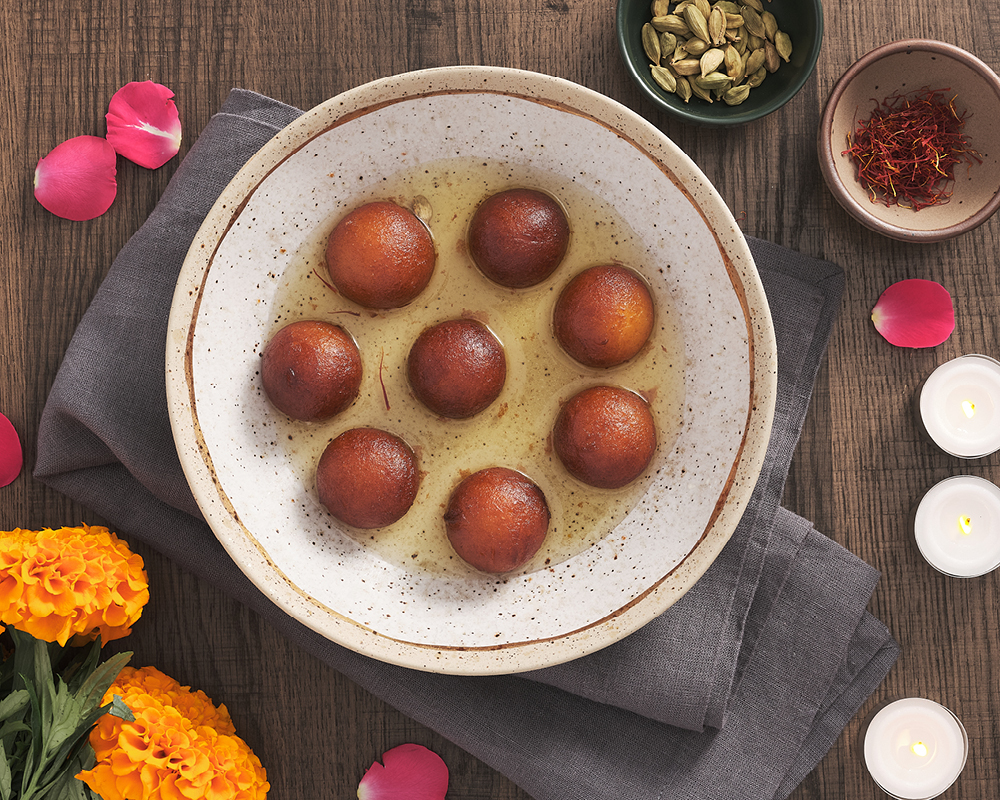 Fried donuts soaked in syrup surrounded by flowers, candles, and spices
