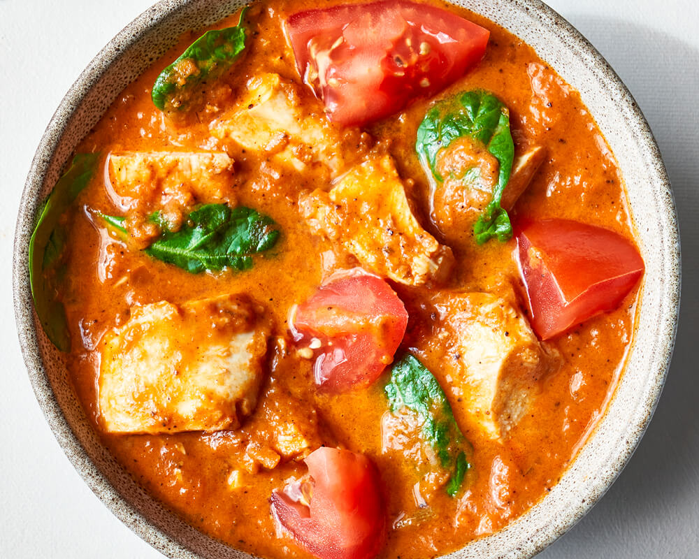 bowl of chicken tikka masala with cubes of chicken, chunks of tomato, and spinach leaves