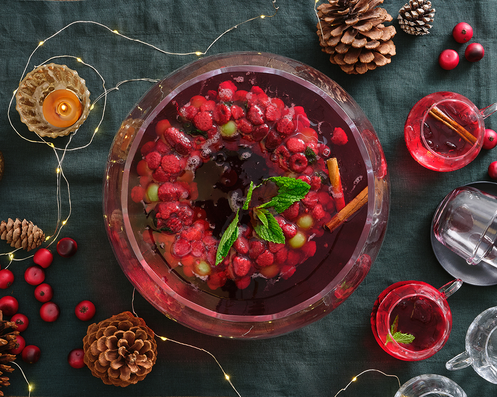 Holiday punch bowl with cups, pinecones, cranberries, and lights