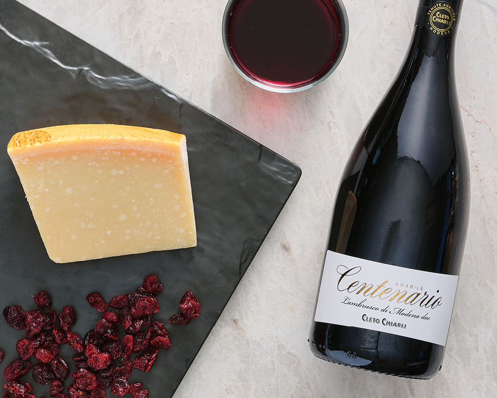 Parmigiano Reggiano Cheese with Dried Cranberries on Black Stone Cutting Board with Amabile Centenario Lambrusco di Modena doc red wine bottle on marble table