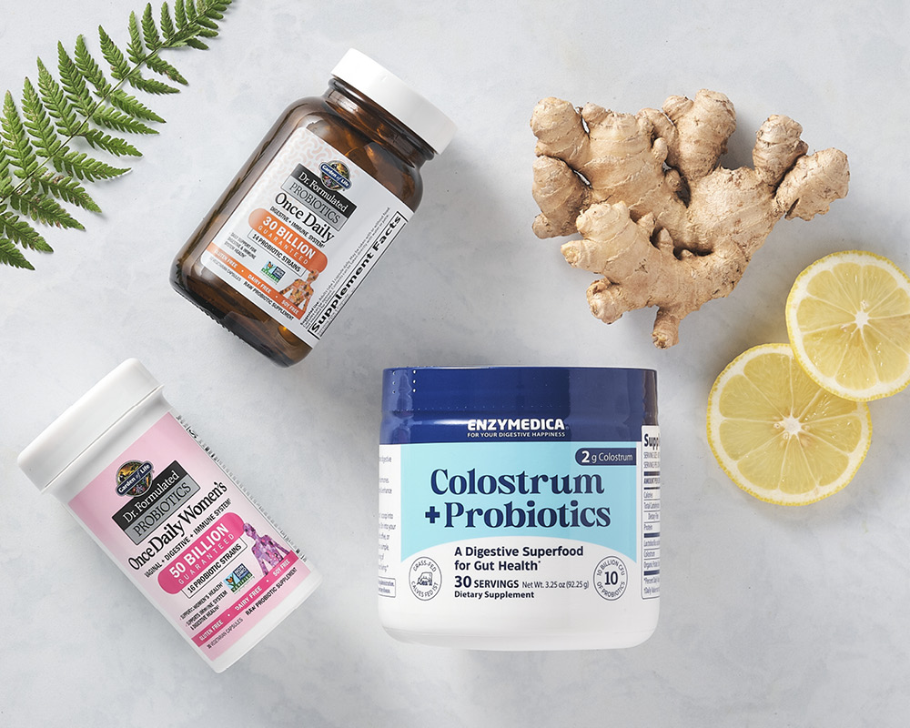 Probiotics and colostrum products styled with lemon slices, ginger, and a fern