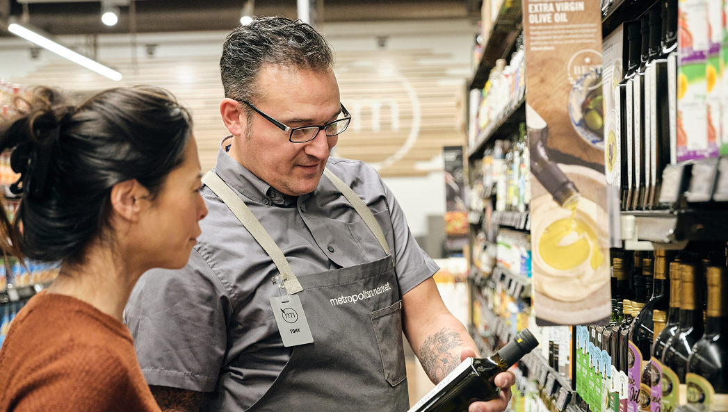 Metropolitan Market team member showing a guest a bottle of Metropolitan Market Extra Virgin Olive Oil