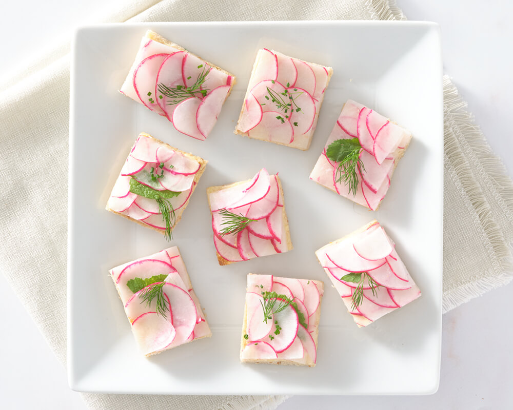 7 square open faced sandwiches layered with thin radish slices and garnished with herbs